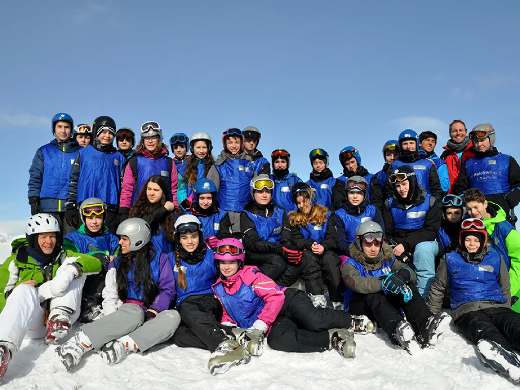 Große Gruppe sitzt und steht für ein Gruppenfoto im Schnee.